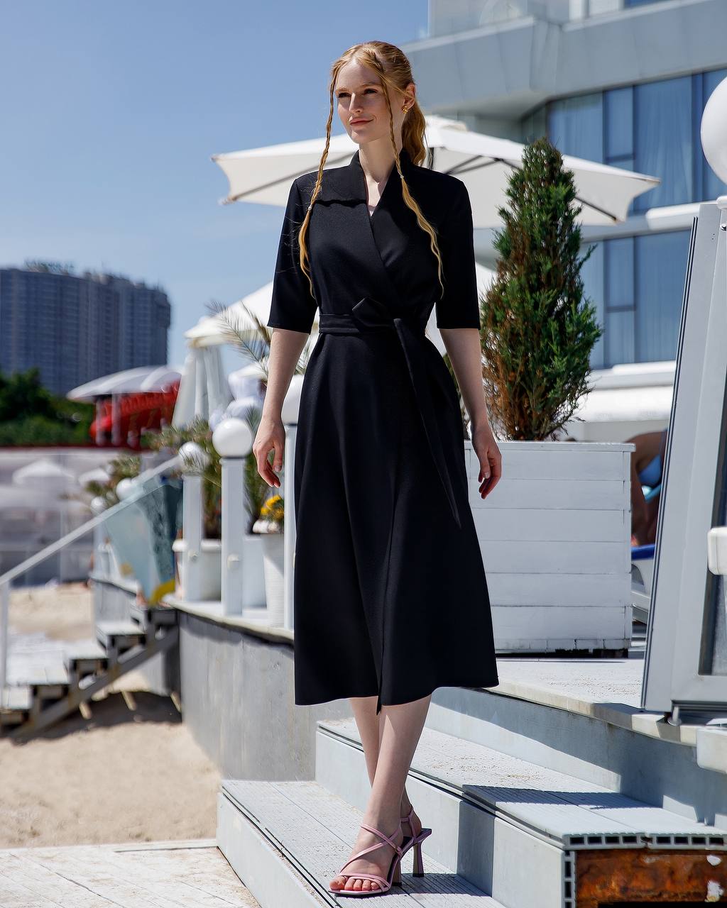 Woman in a black dress standing on a rooftop with buildings and plants in the background