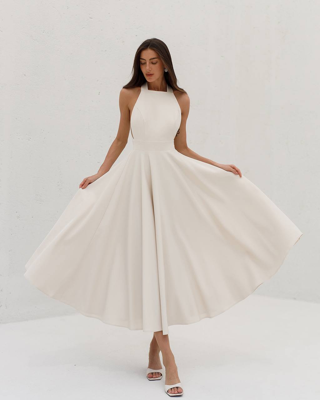 Woman wearing a white halter neck dress against a plain background