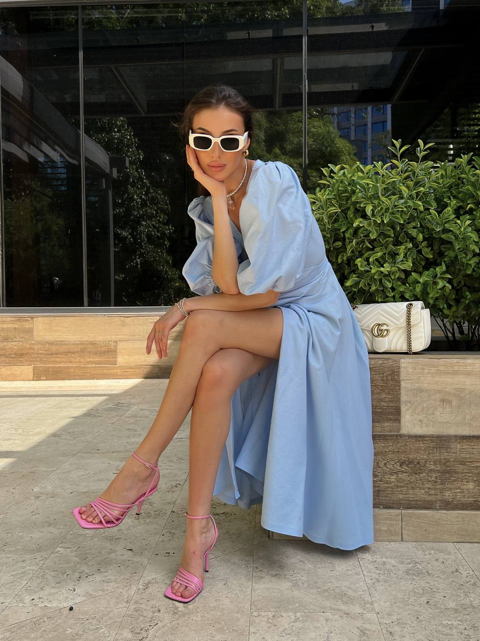 Woman in a light blue dress and pink heels sitting outdoors.