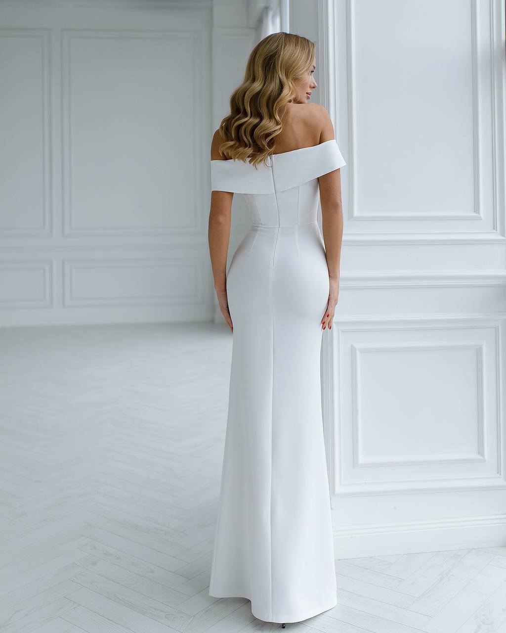Woman wearing a white off-shoulder gown in a minimalistic room.