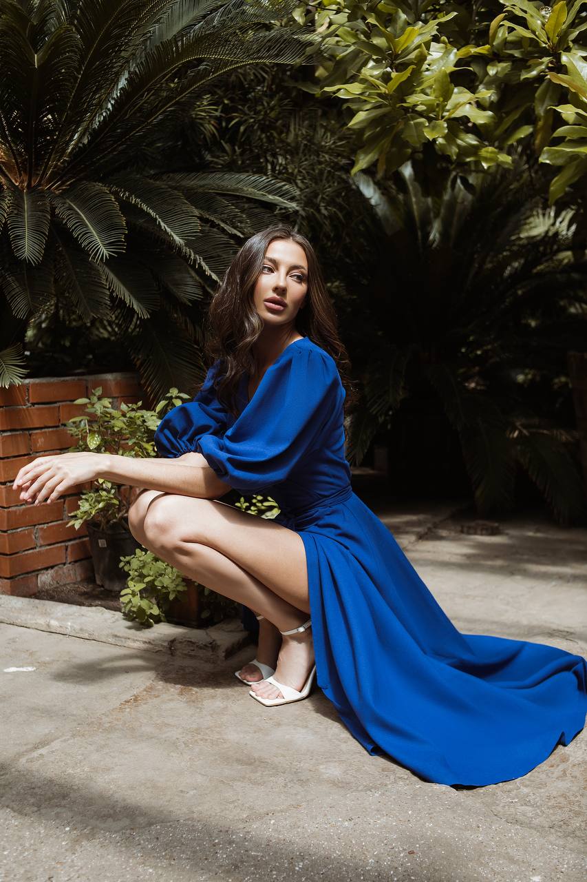 Woman in a blue dress sitting outdoors with greenery around