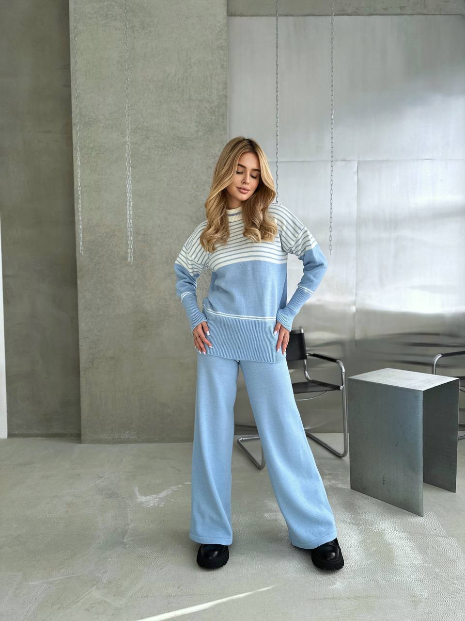 Woman wearing a light blue and gray striped sweater with matching pants in a modern room.