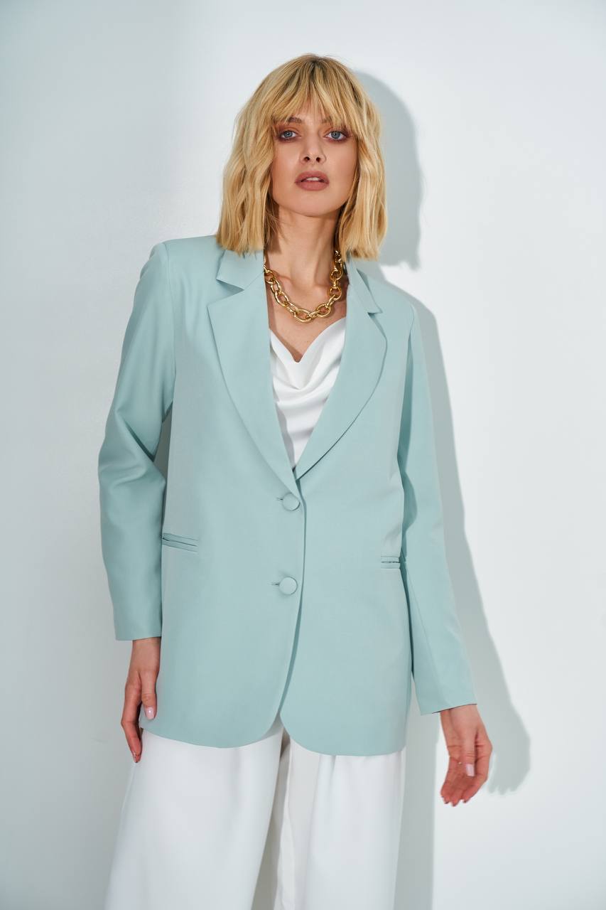 Woman wearing a light blue blazer over a white top and pants on a plain background