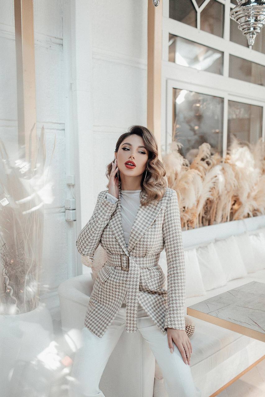 Woman in a plaid coat standing in a stylish interior setting with decorative plants.