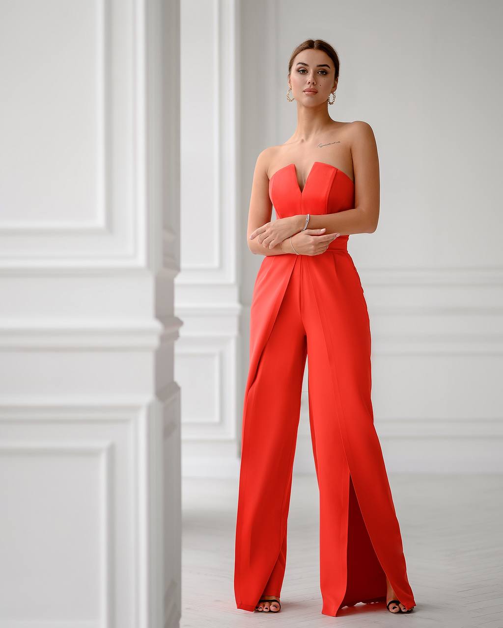 Woman wearing a red strapless jumpsuit against a white wall