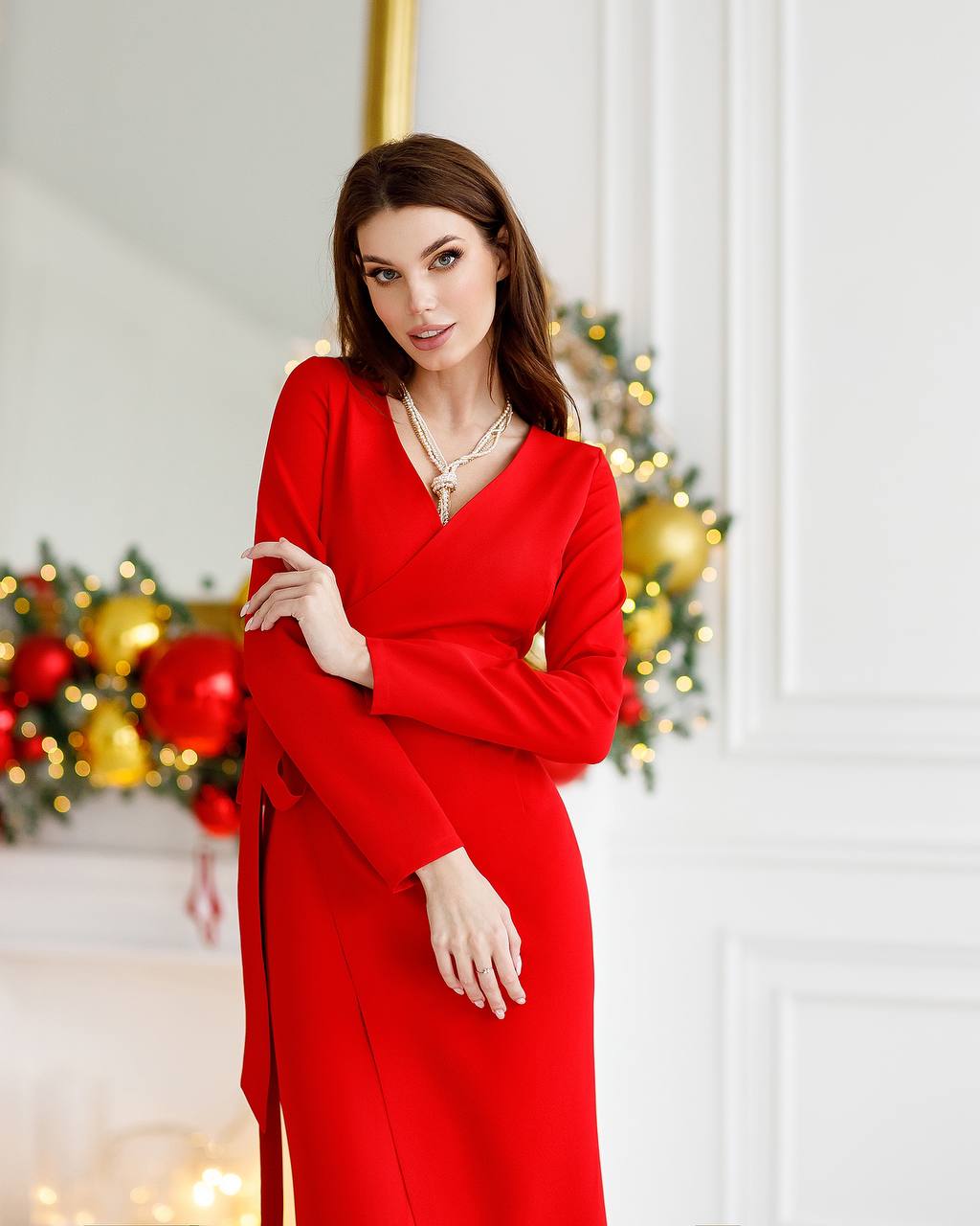 Woman in a red dress standing in front of a decorated Christmas fireplace.