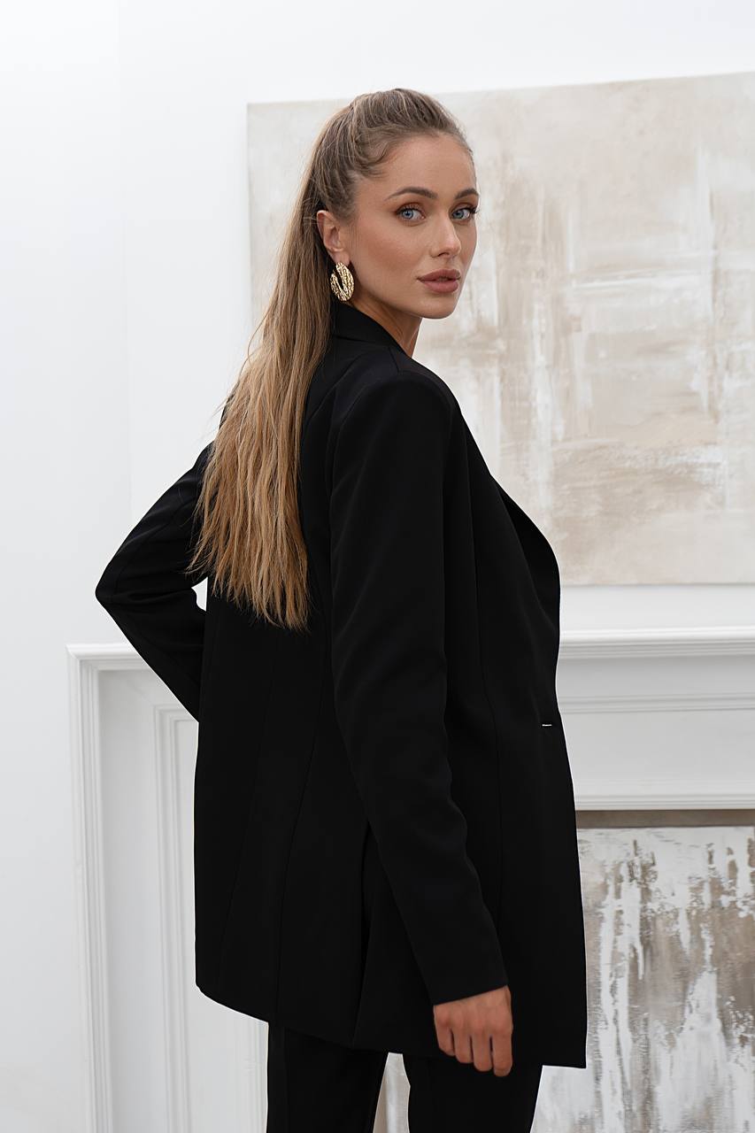 Woman wearing a black blazer in an indoor setting with abstract art on the wall.