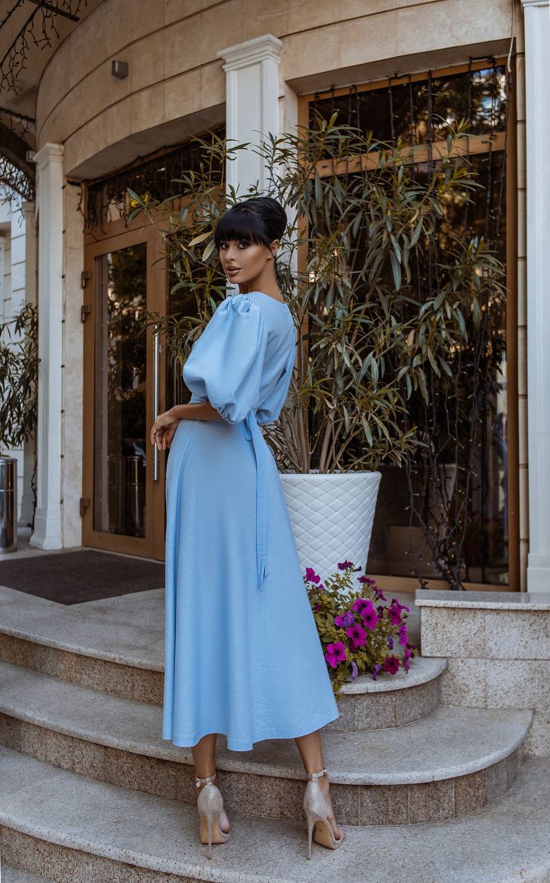 Woman in a light blue dress standing on steps outside a building with plants and flowers.