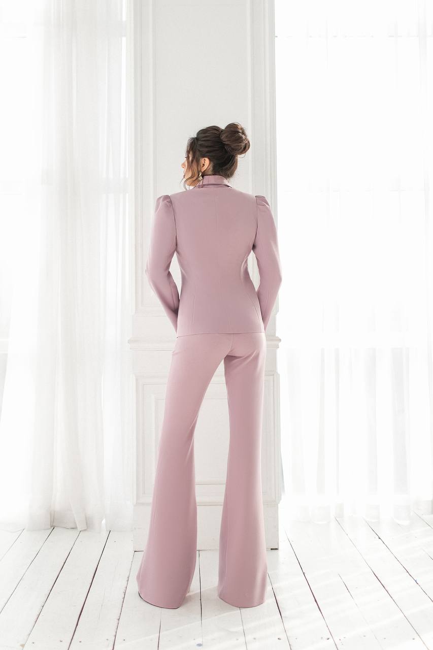 Woman wearing a pink suit standing in front of white curtains.