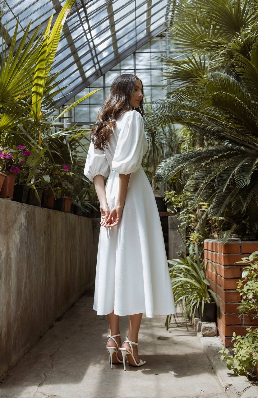 Woman in a white dress standing in a greenhouse filled with plants