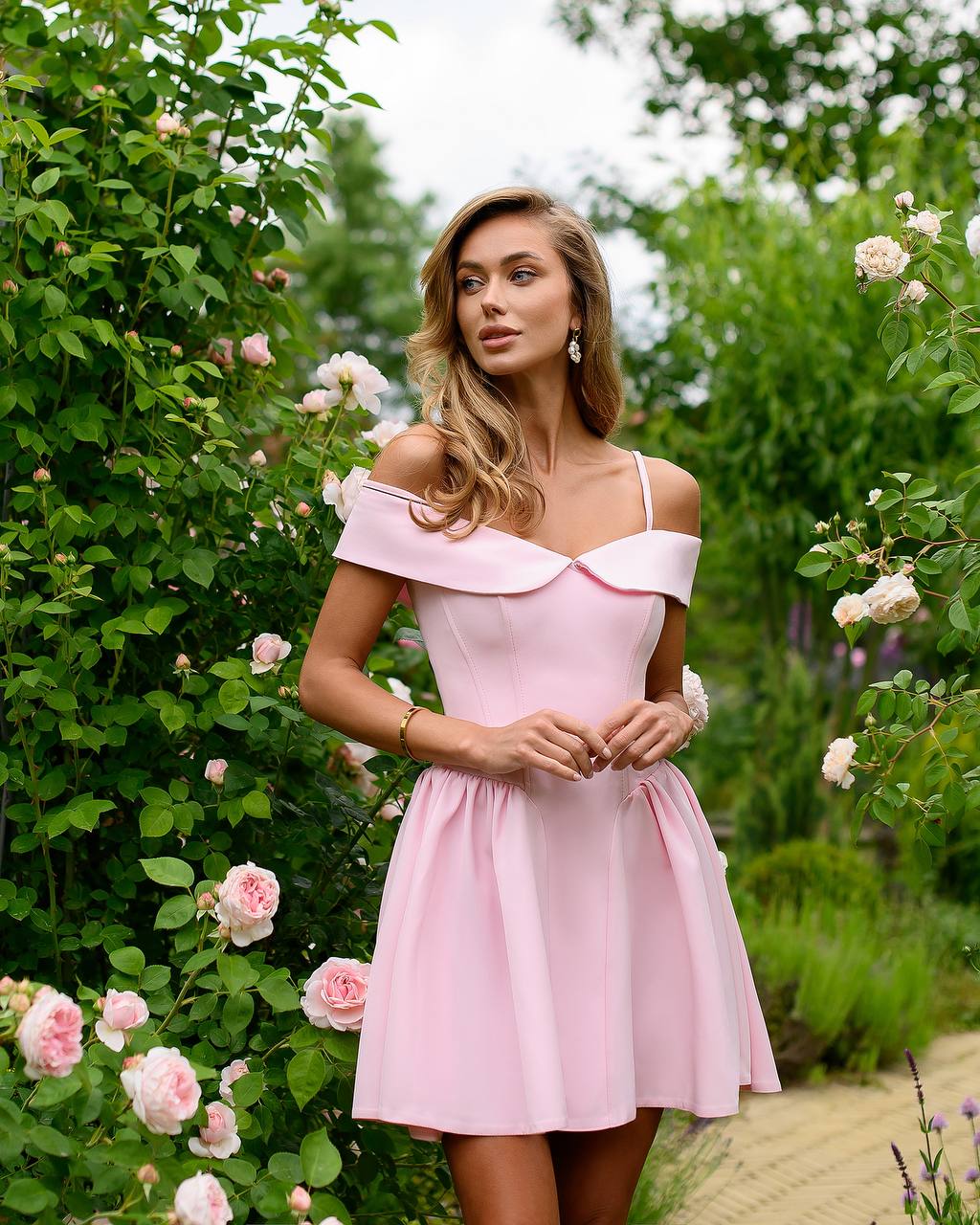 Woman in a pink dress standing in a garden with flowers and greenery.