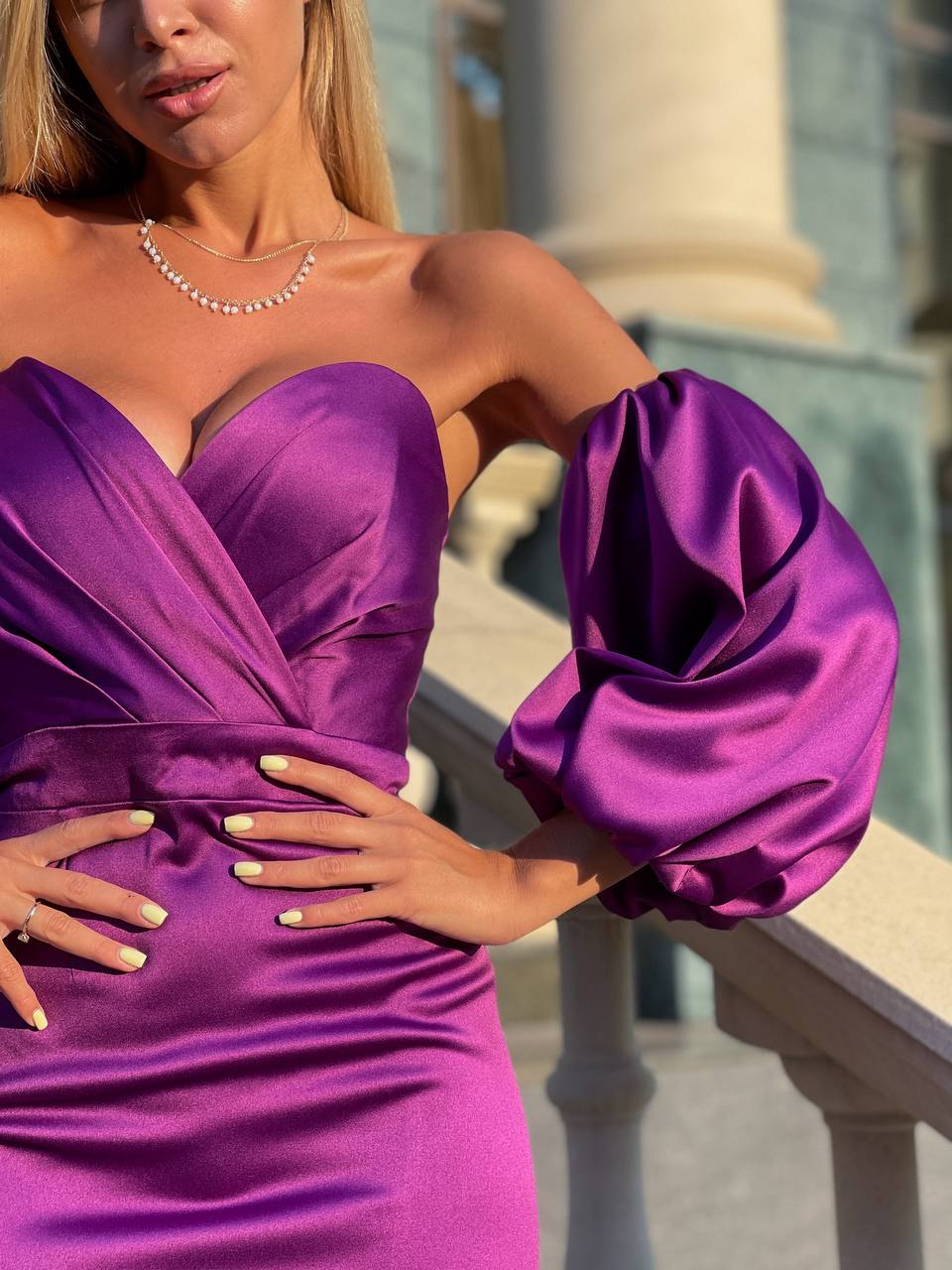 Woman wearing a purple dress with puffed sleeves standing outdoors.