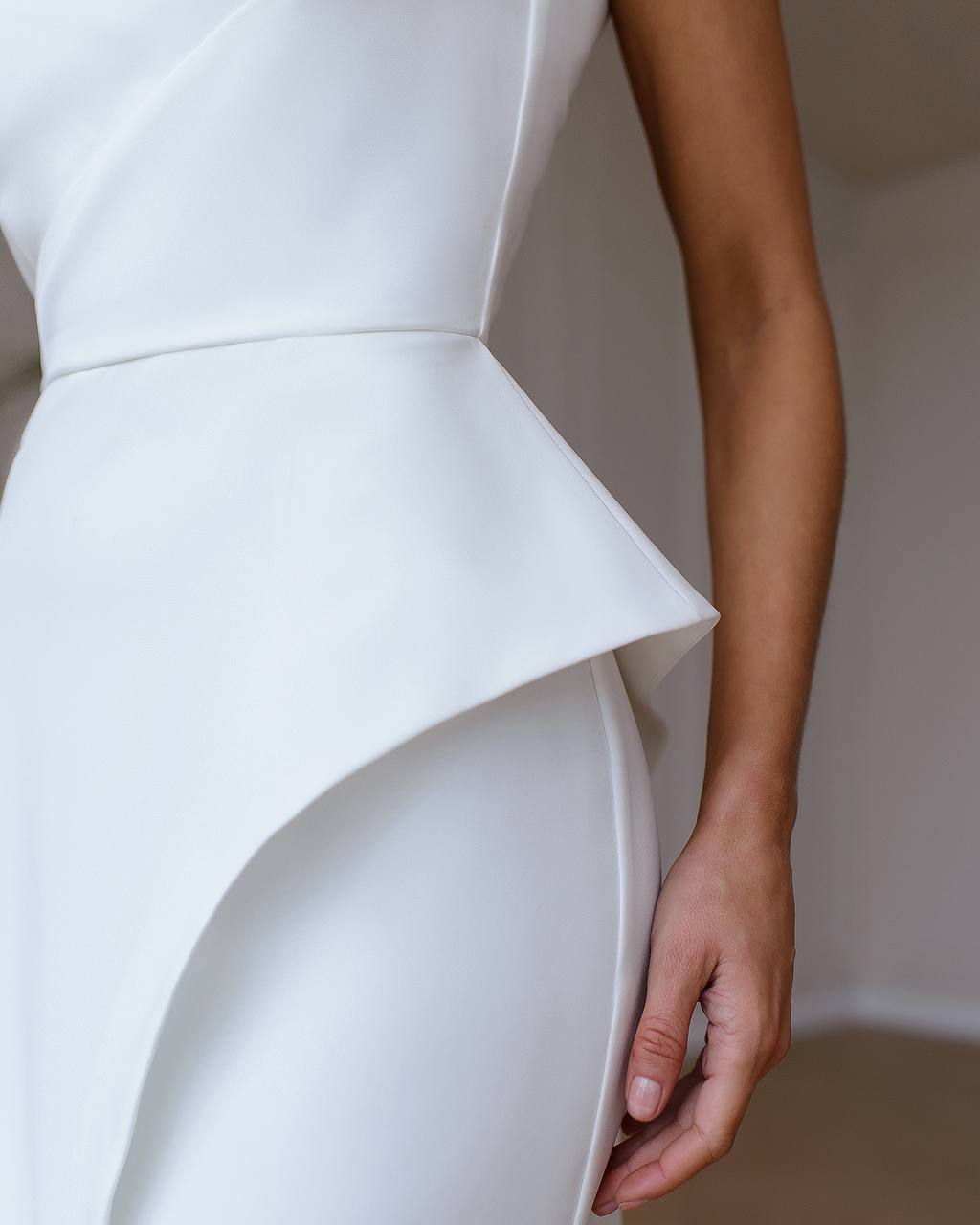 Close-up of a white dress with a peplum detail on a plain background