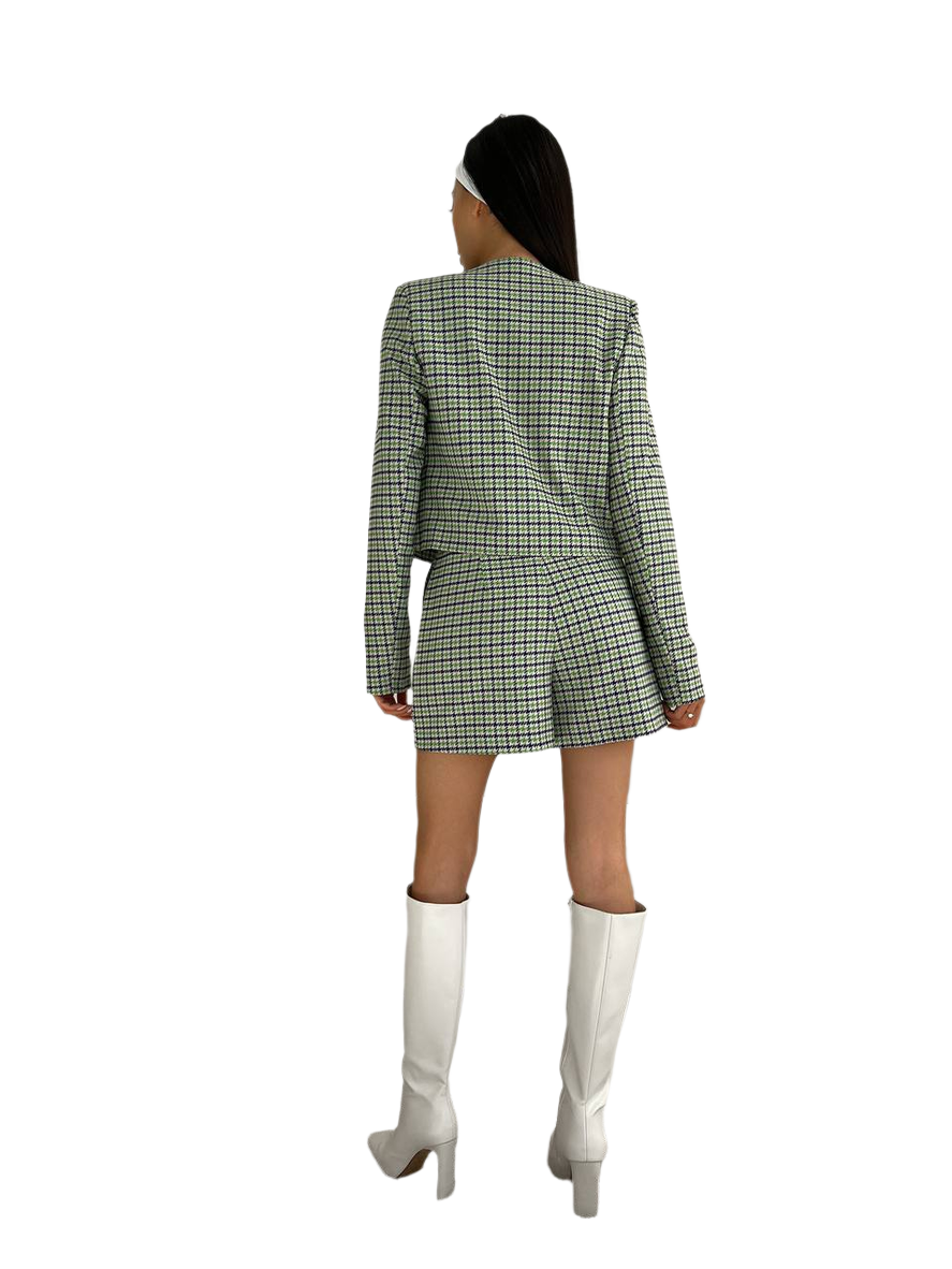 Person wearing a green checkered blazer dress with white knee-high boots on a white background