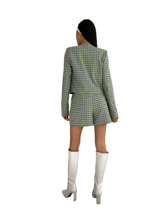 Person wearing a green checkered blazer dress with white knee-high boots on a white background