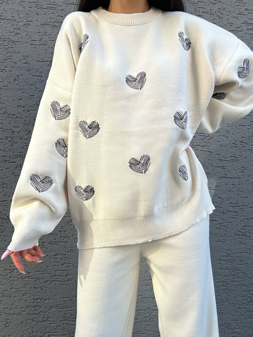 White sweater with black heart patterns worn by a person against a gray background
