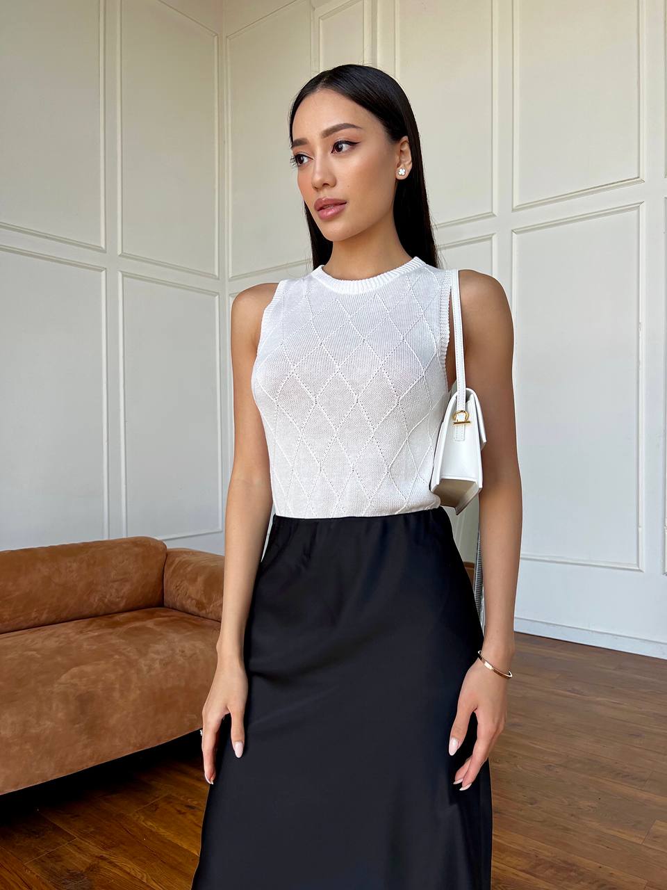 Woman wearing a white top and black skirt in a room with a brown couch.
