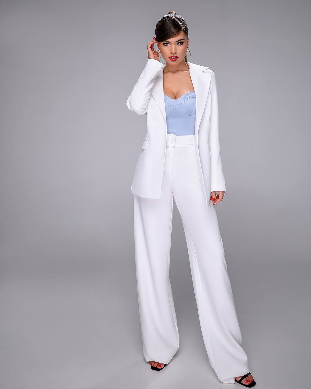 Woman wearing a white suit with a light blue top on a gray background