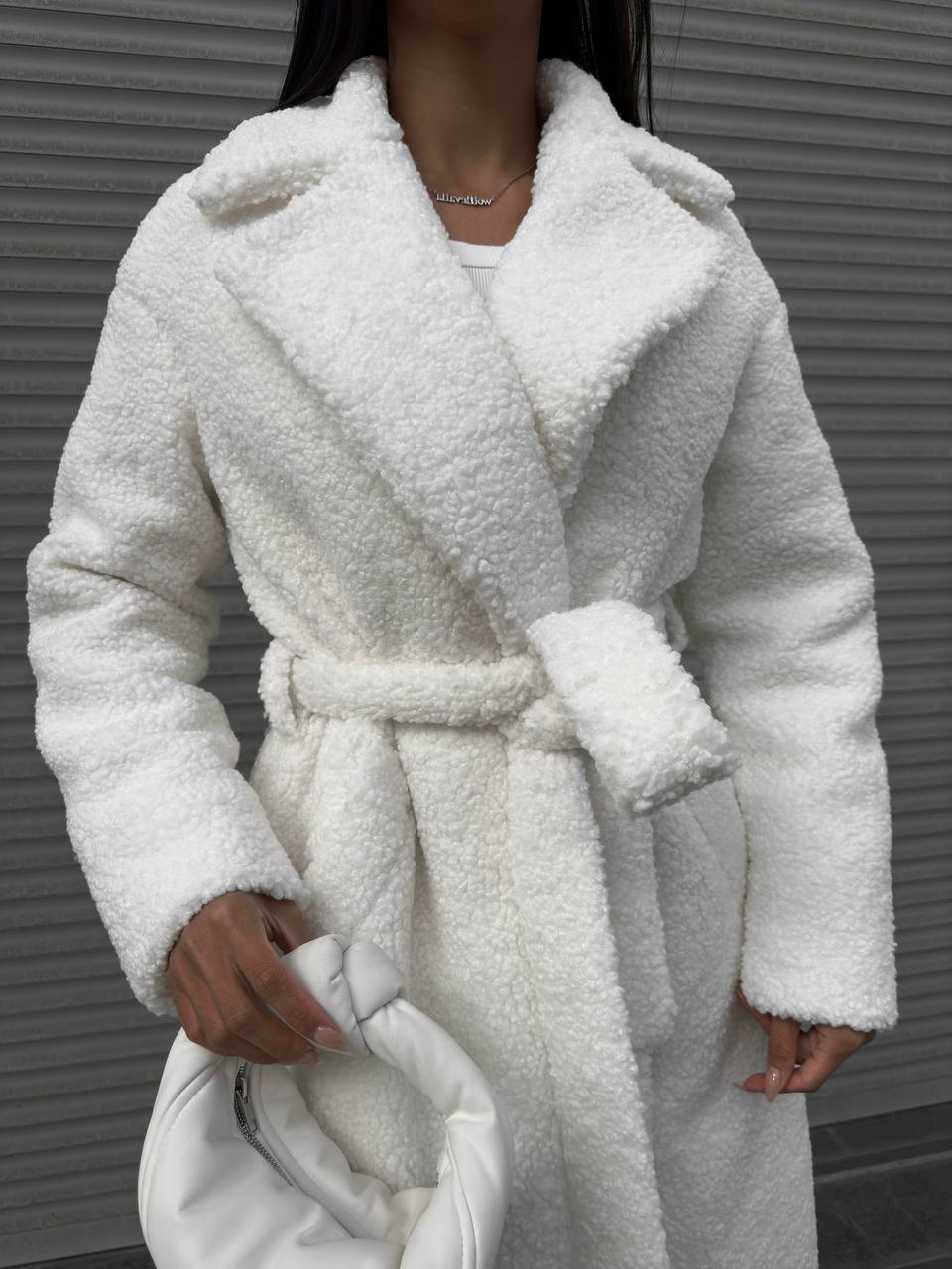 White fluffy coat worn by a person against a gray background