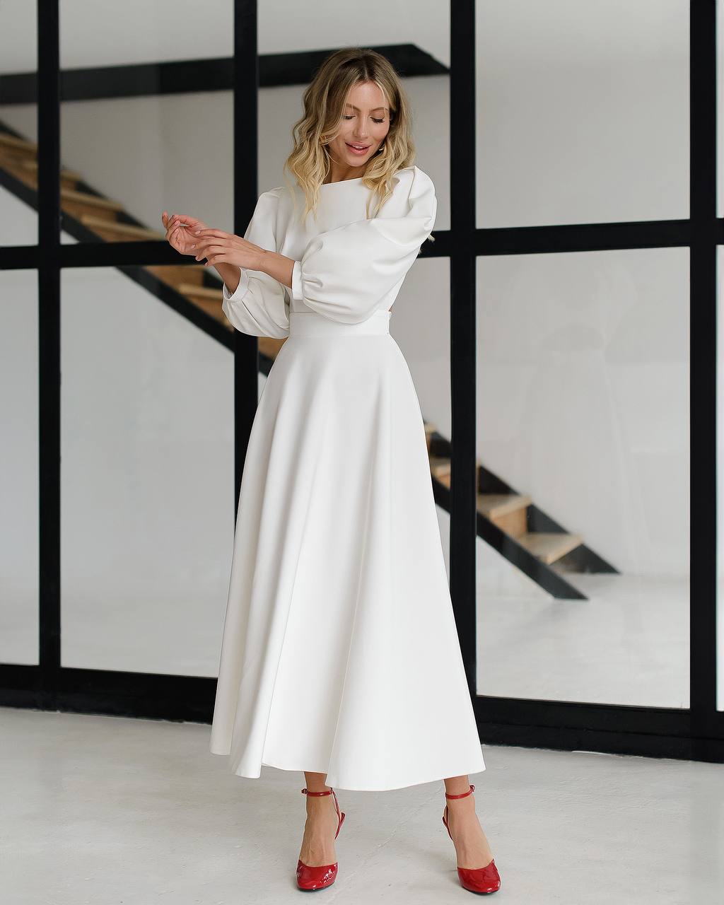 Woman in a white dress standing in a modern interior setting with a staircase.