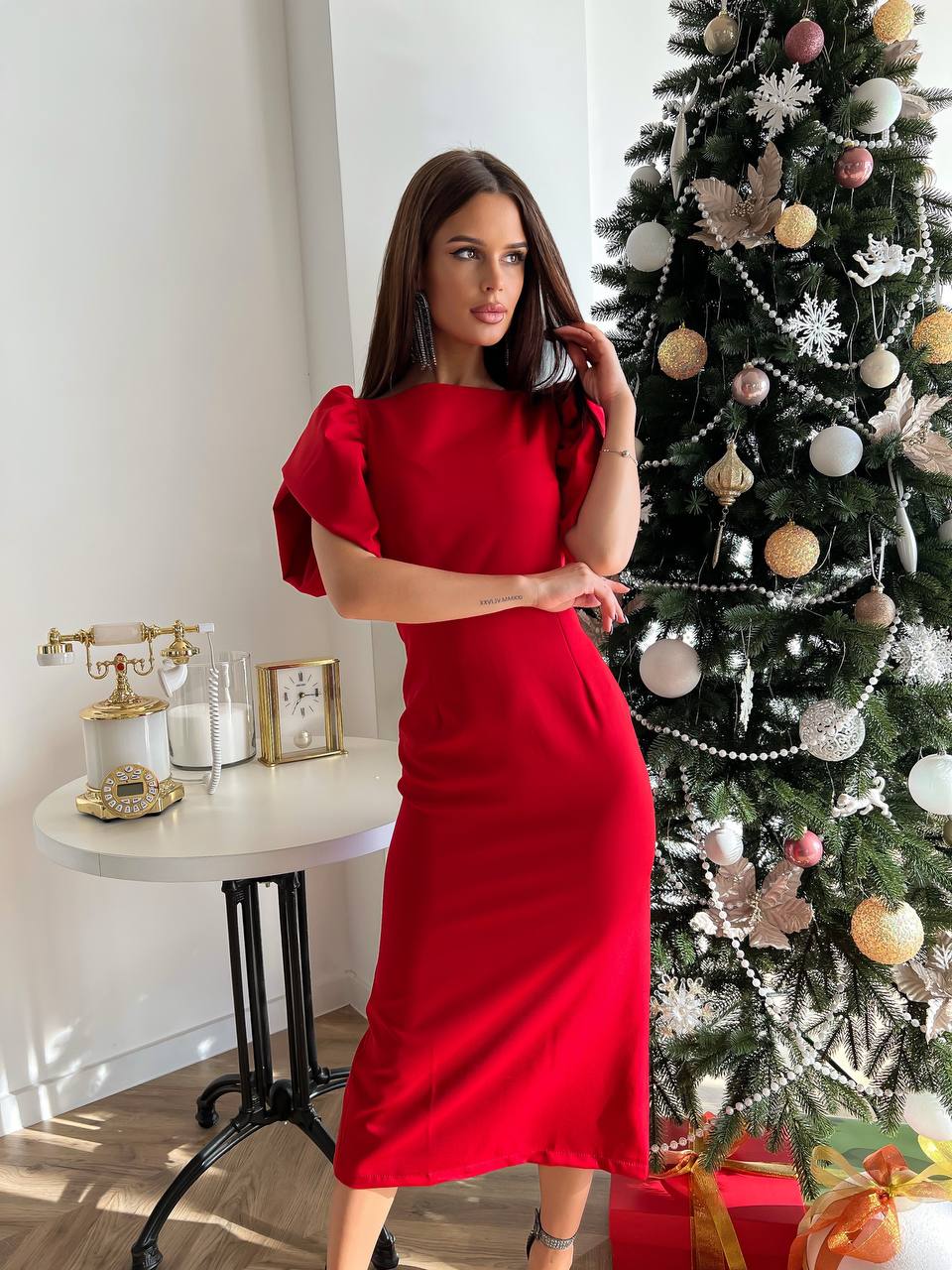 Woman in a red dress standing next to a decorated Christmas tree indoors.