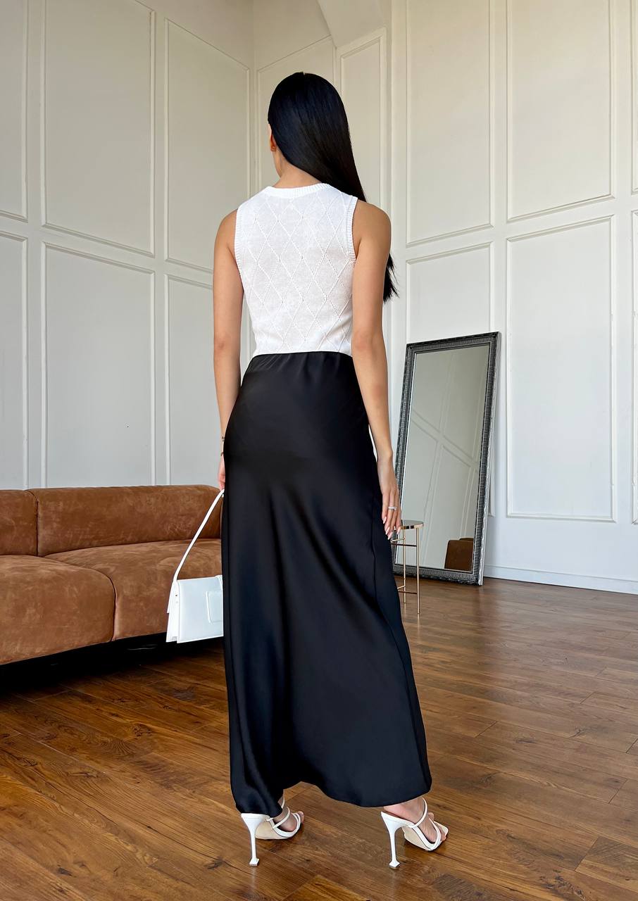 Woman wearing a white top and black skirt standing in a room with a brown couch and mirror.