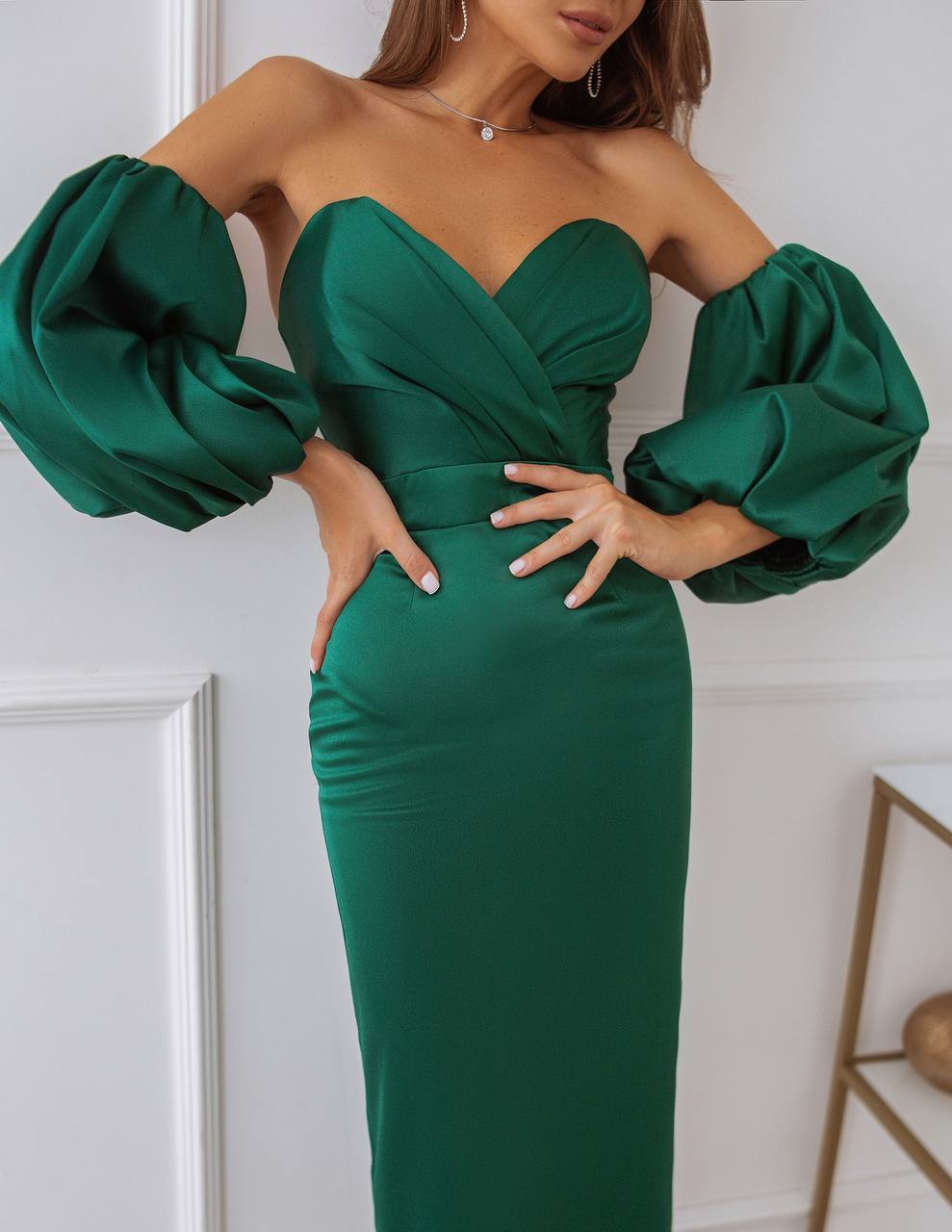 Green strapless dress with puffed sleeves worn by a model against a white wall.