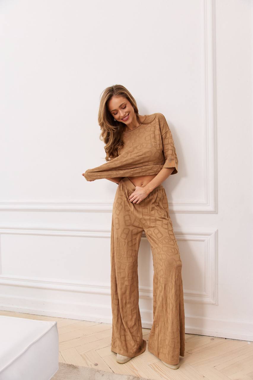 Woman wearing a brown outfit standing against a white wall.