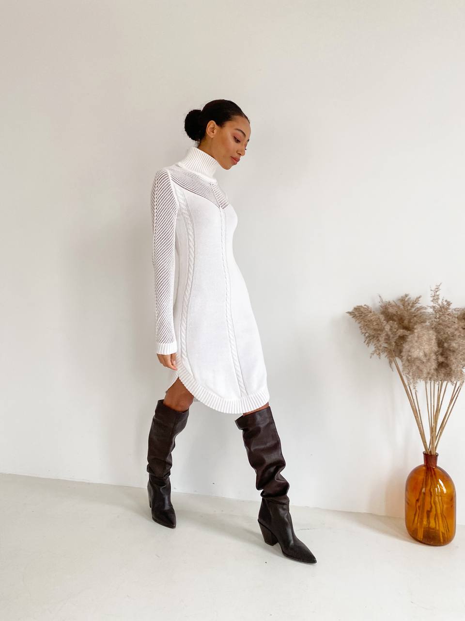 Woman wearing a white dress and brown knee-high boots against a plain background