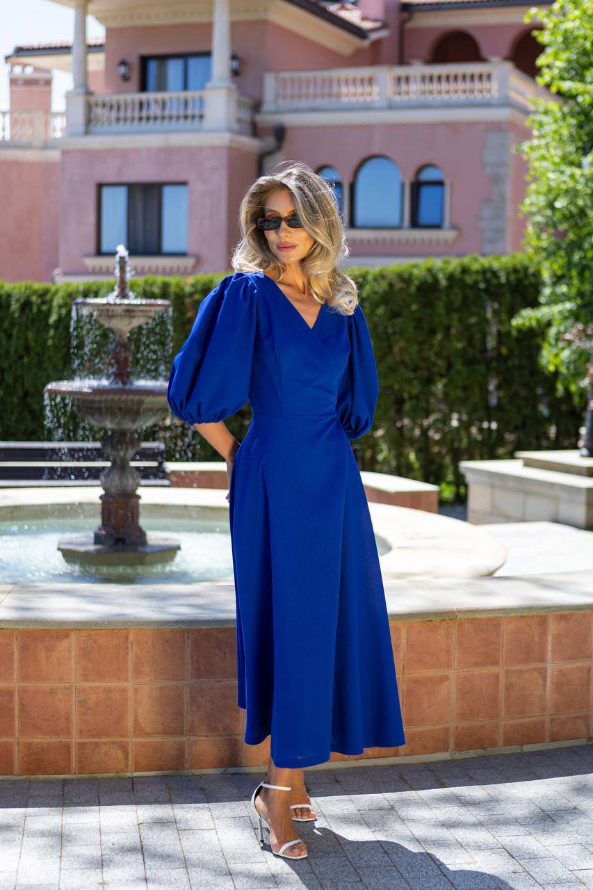 Woman in a blue dress standing in front of a fountain with a pink building in the background