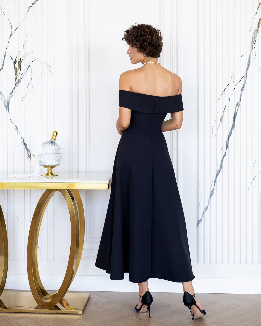 Woman wearing a black off-shoulder dress in an elegant interior setting.