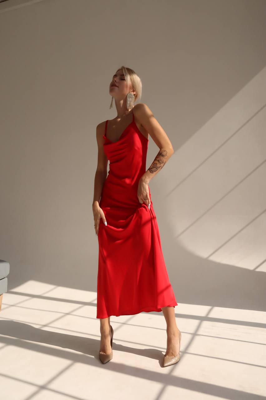 Woman in a red dress standing in a sunlit room with shadows on the wall.