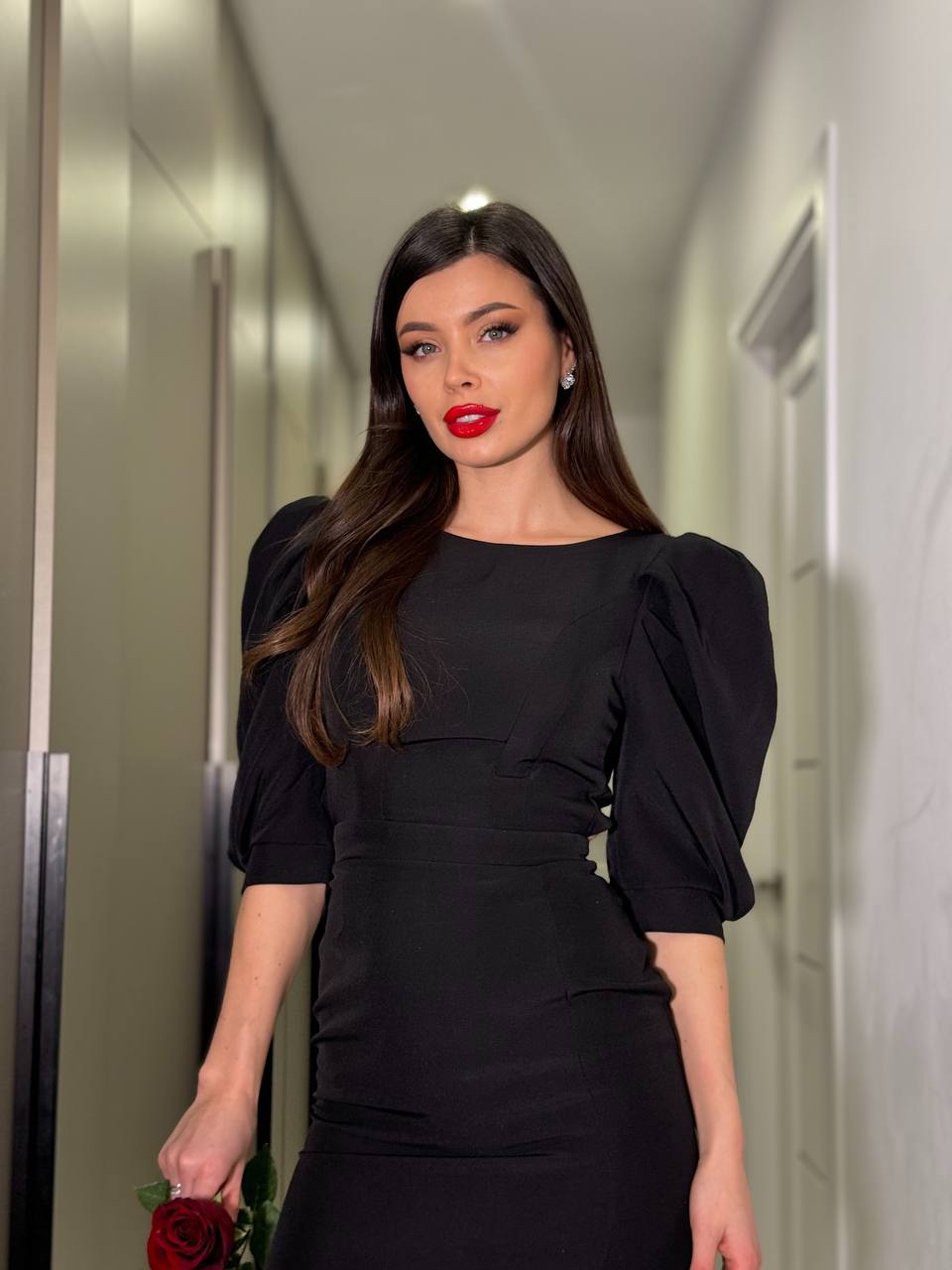 Woman in a black dress with puffed sleeves standing in a hallway.