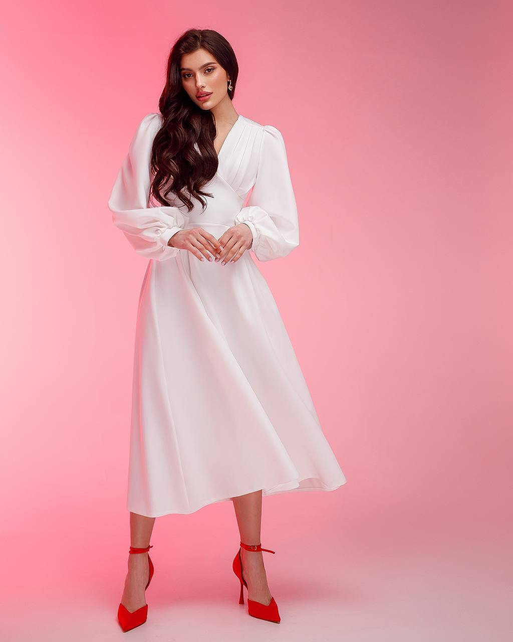 Woman wearing a white dress with long sleeves against a pink background