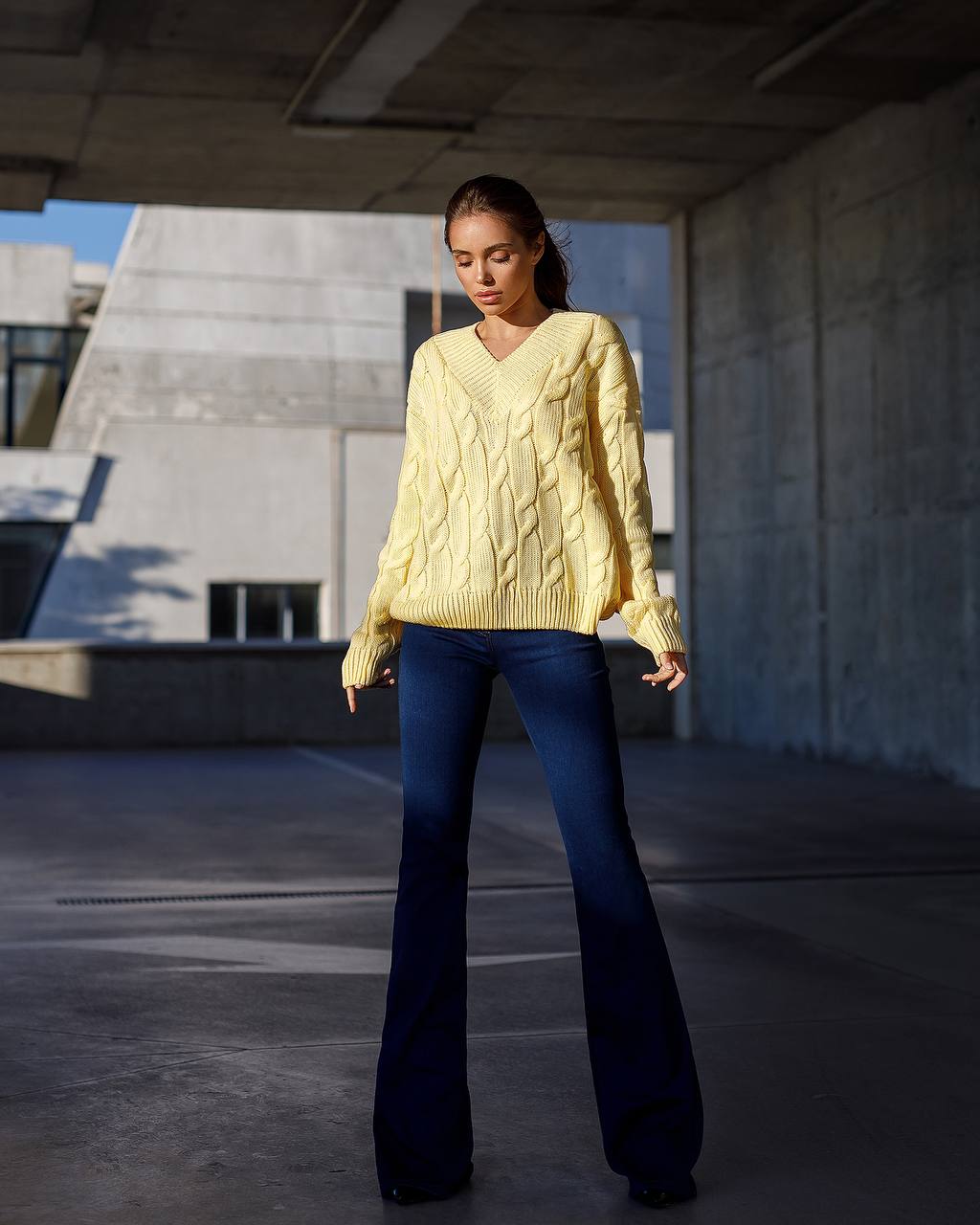 Woman wearing a yellow cable knit sweater and blue flared jeans standing in an urban setting.