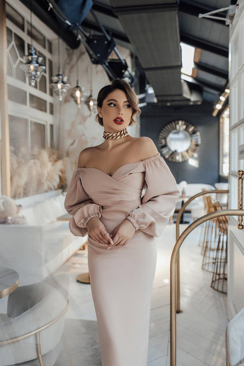 Woman in a pink off-shoulder dress standing in an elegant interior setting.