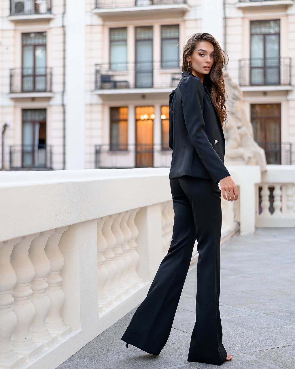 Woman in a black suit standing on a balcony with classical architecture in the background