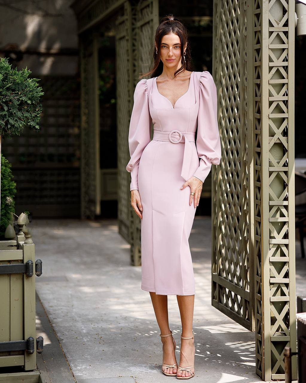 Woman in a light pink dress standing in an outdoor setting with decorative elements.