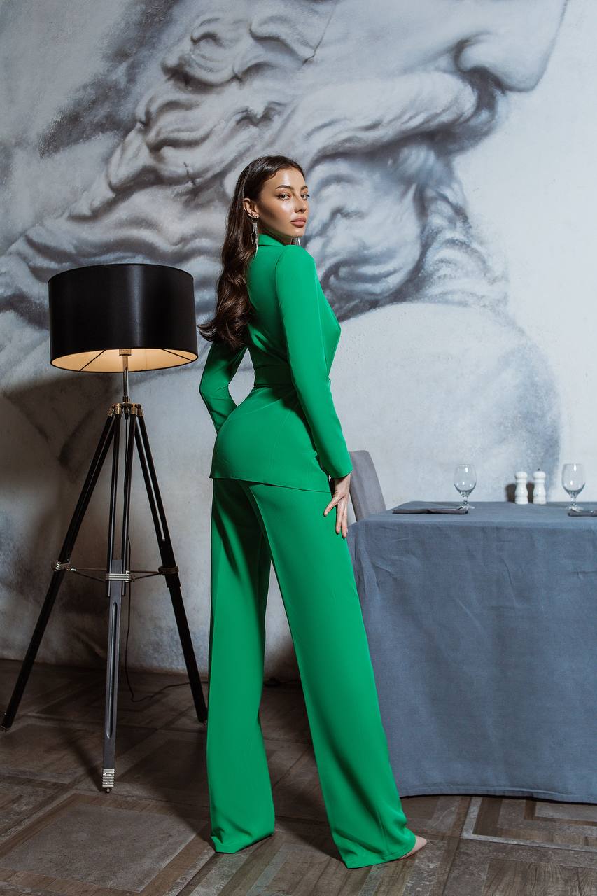 Woman in a green outfit standing in a room with a lamp and table.