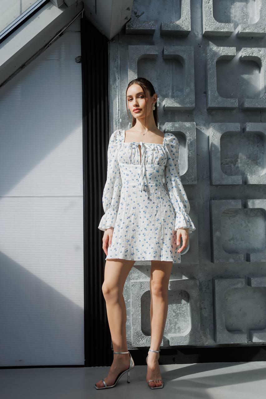 Woman in a floral dress standing against a textured wall.