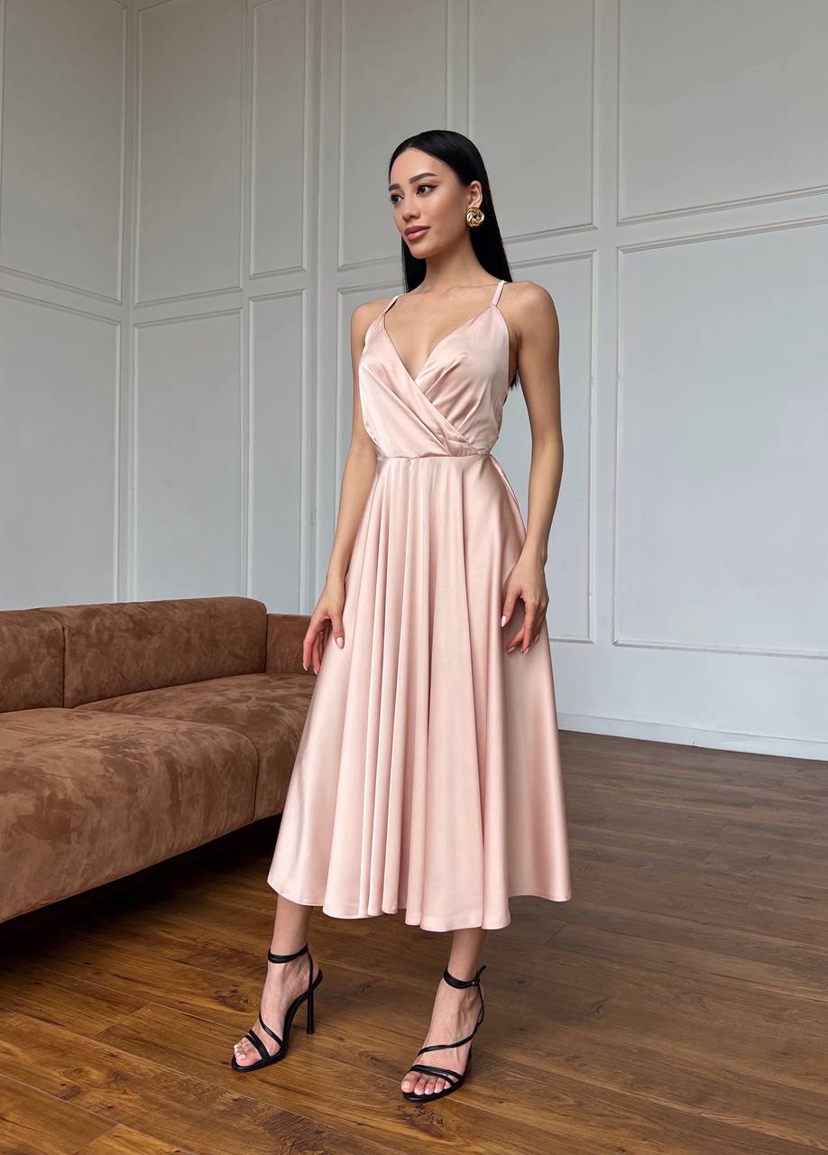 Woman wearing a pink dress standing in a room with a brown sofa and white paneled walls.