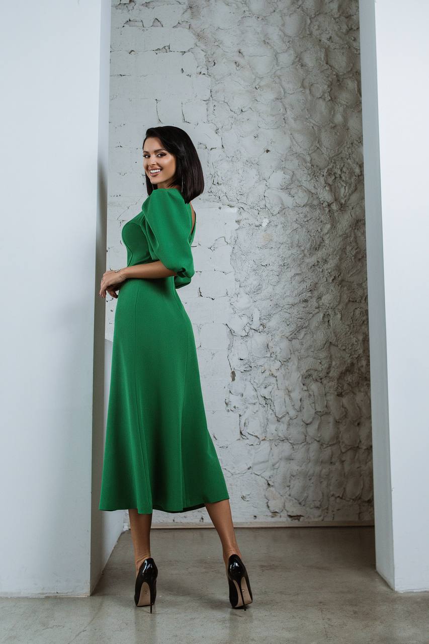 Woman in a green dress standing against a textured wall.
