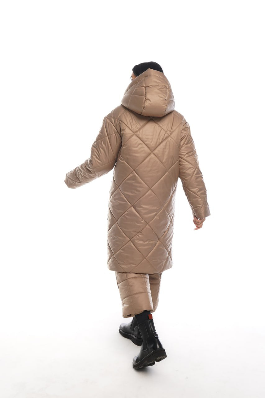 Person wearing a long beige quilted coat on a white background