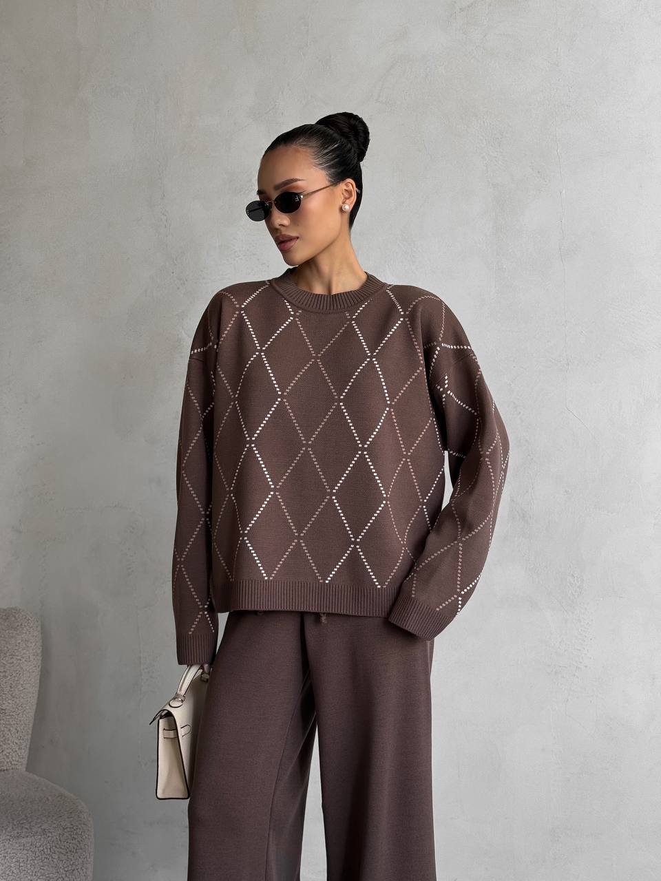 Woman wearing a brown patterned sweater and pants against a gray background