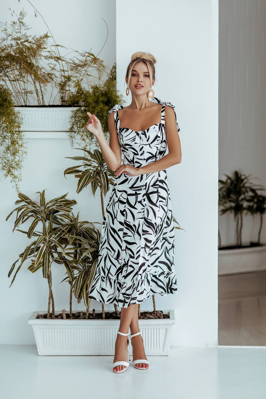 Woman in a black and white dress standing in front of potted plants.