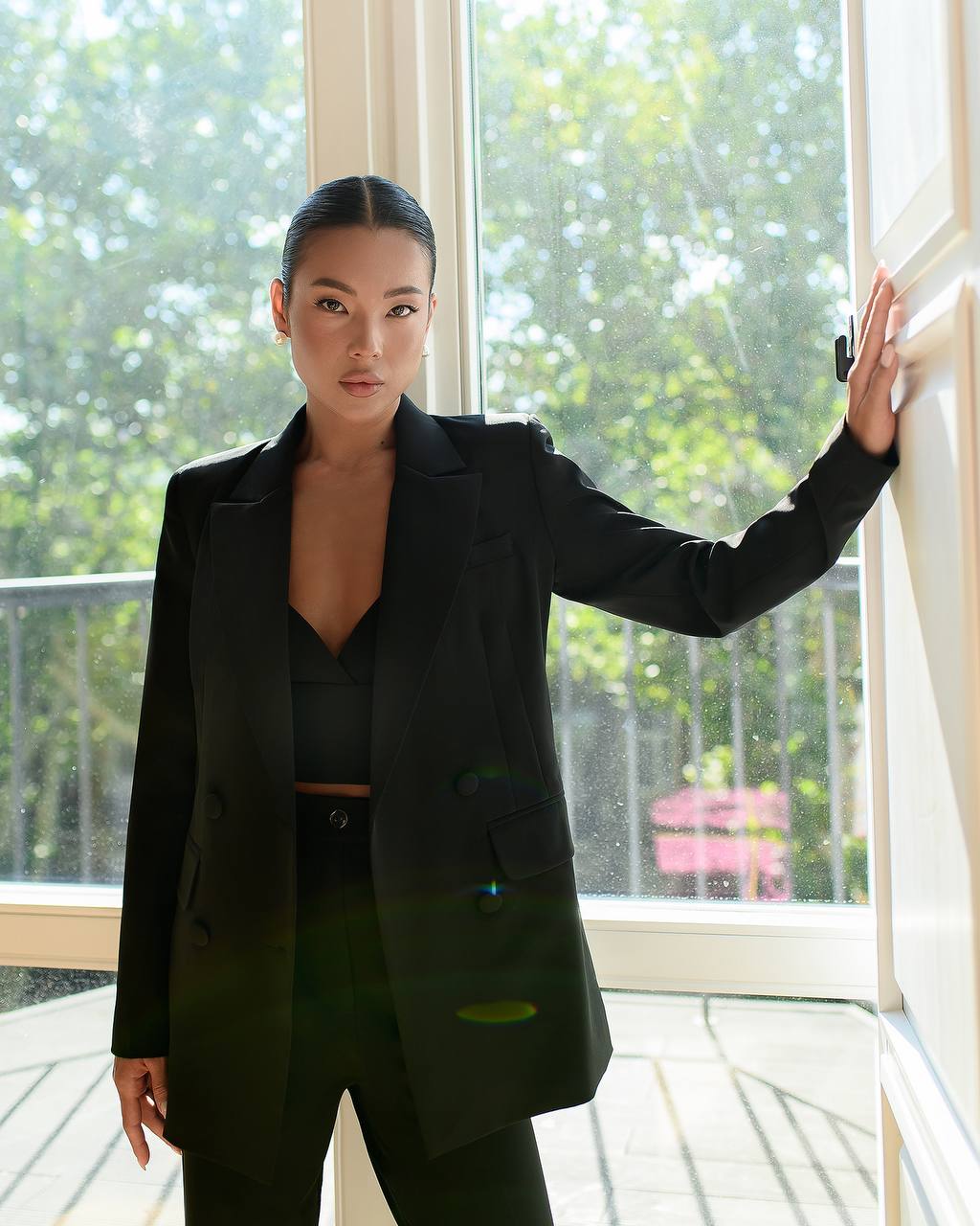 Person wearing a black blazer and green top in front of a window with greenery outside