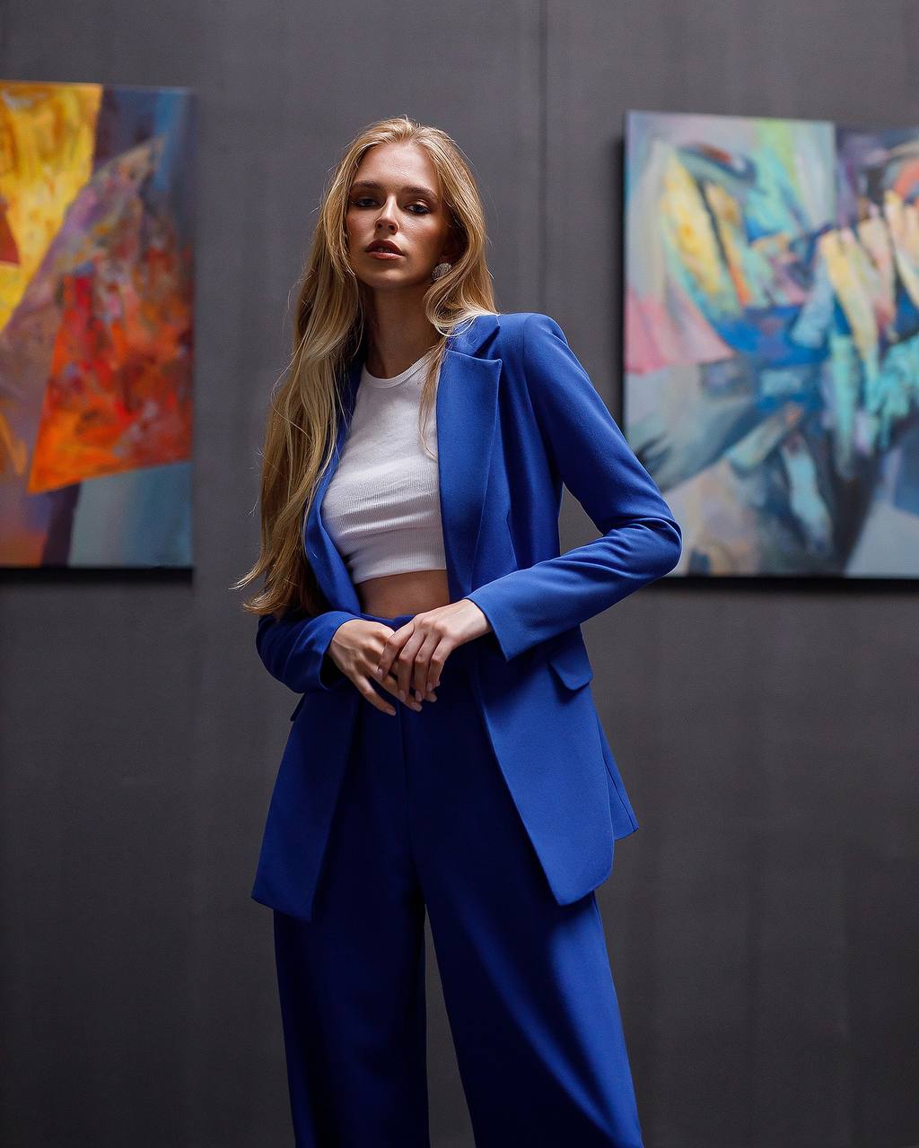 Woman in a blue suit standing in front of colorful abstract paintings.