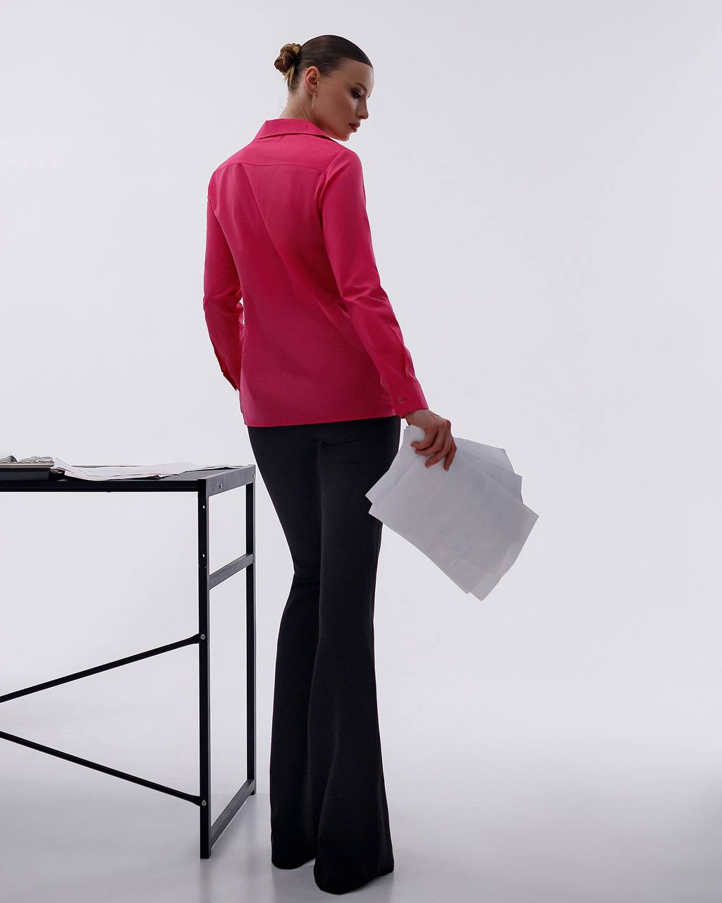 Person wearing a pink blazer and black pants holding papers on a white background