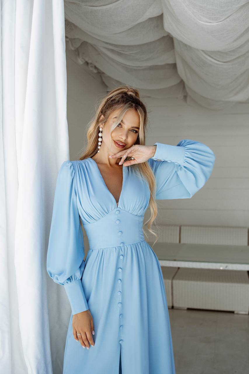 Woman wearing a light blue dress with long sleeves in an indoor setting.