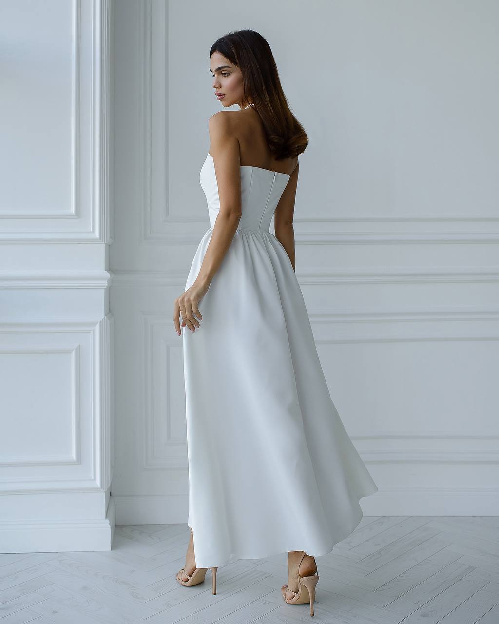 Woman wearing a white strapless dress in a minimalistic room.